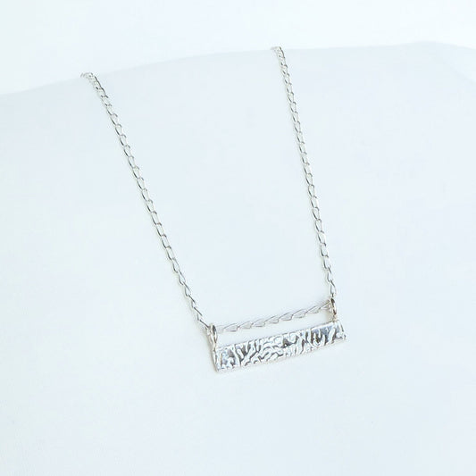 A silver-colored bar necklace with a cuttlefish textured design, displayed against a white background.