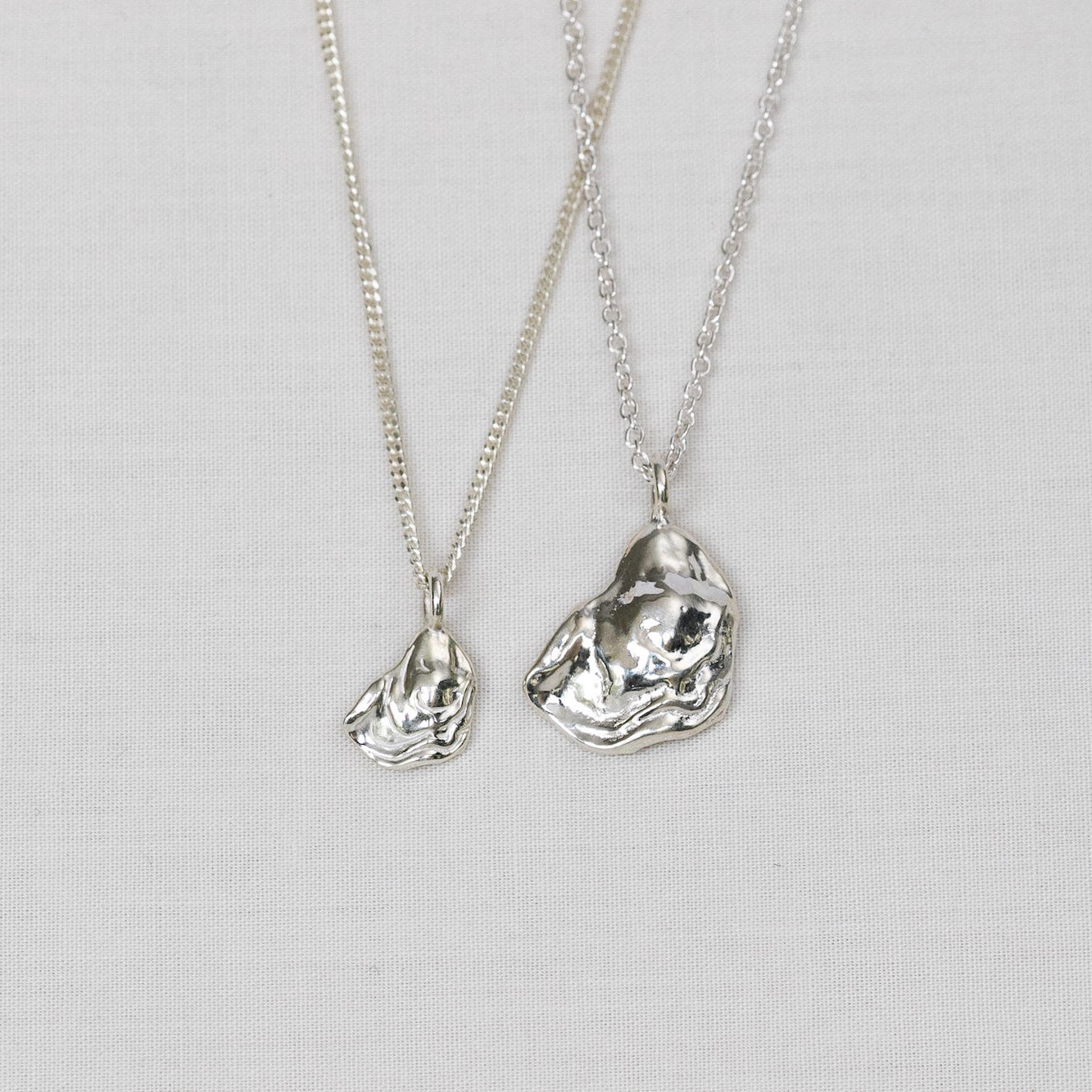 Two silver necklaces with oyster lid pendants on a light background.