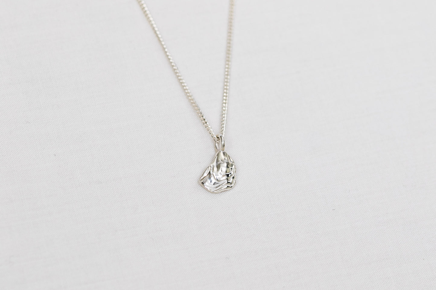A small silver oyster pendant necklace on a light background
