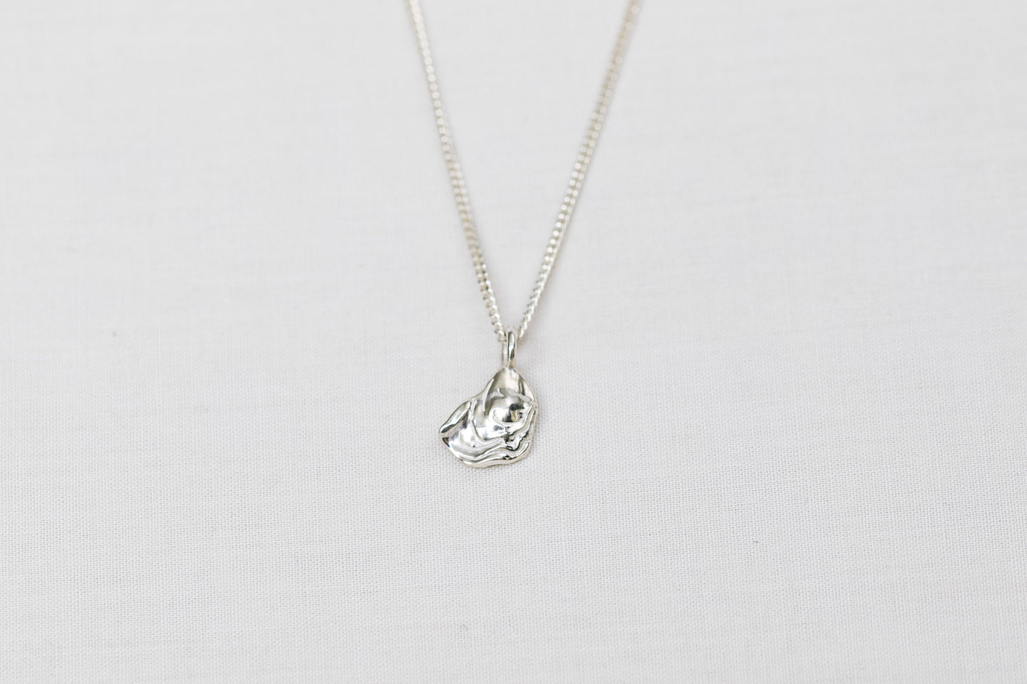 Mini sterling silver oyster pendant necklace sits centred on a light background