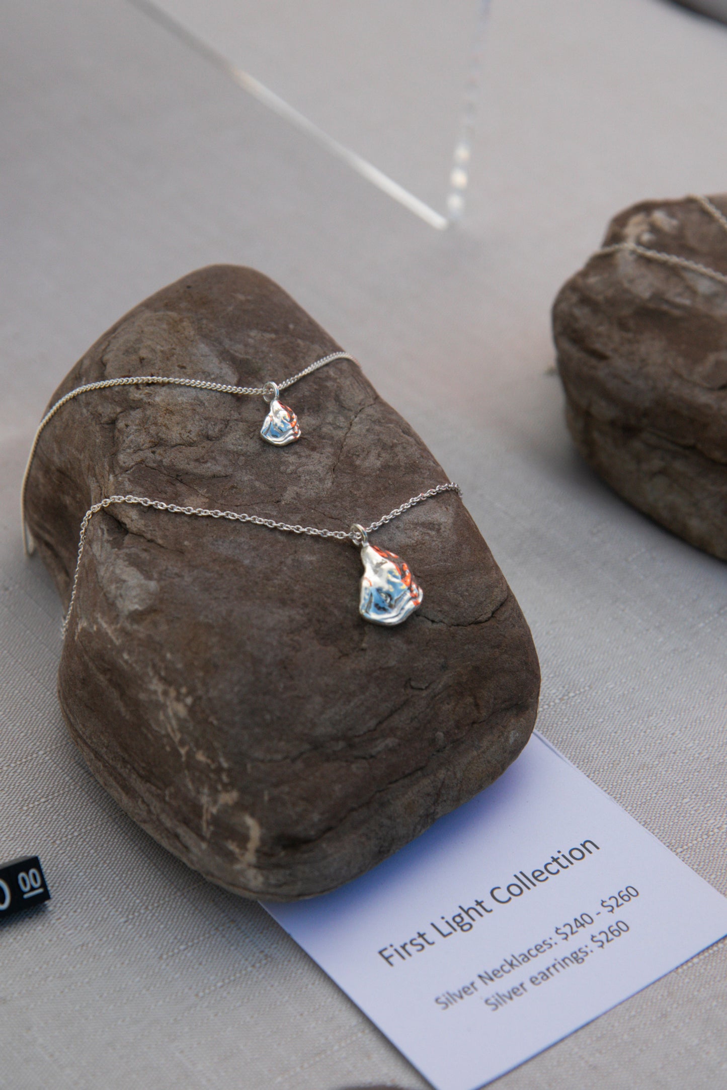 Two silver oyster necklaces lay on a rock, one larger than the other, handcrafted from sterling silver