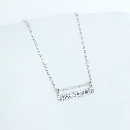 A silver-colored bar necklace with a cuttlefish textured design, displayed against a white background.