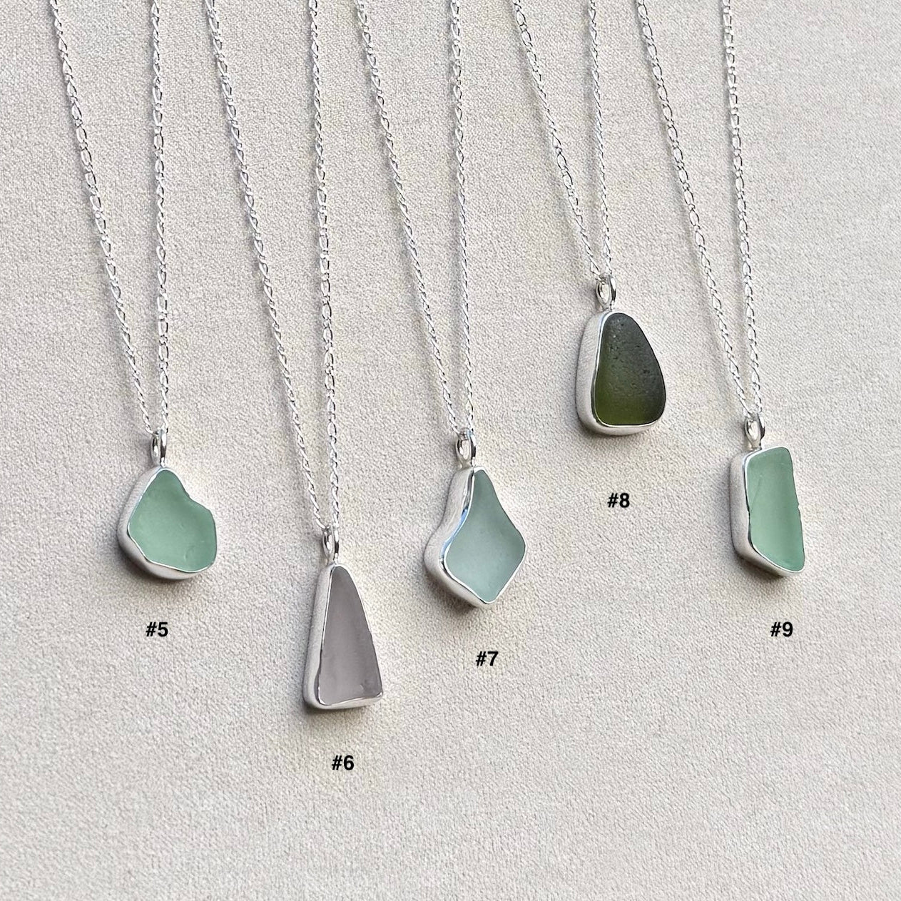 Australian sea glass of various colours set in sterling silver bezels hang from silver chains on plain background