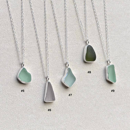 Australian sea glass of various colours set in sterling silver bezels hang from silver chains on plain background
