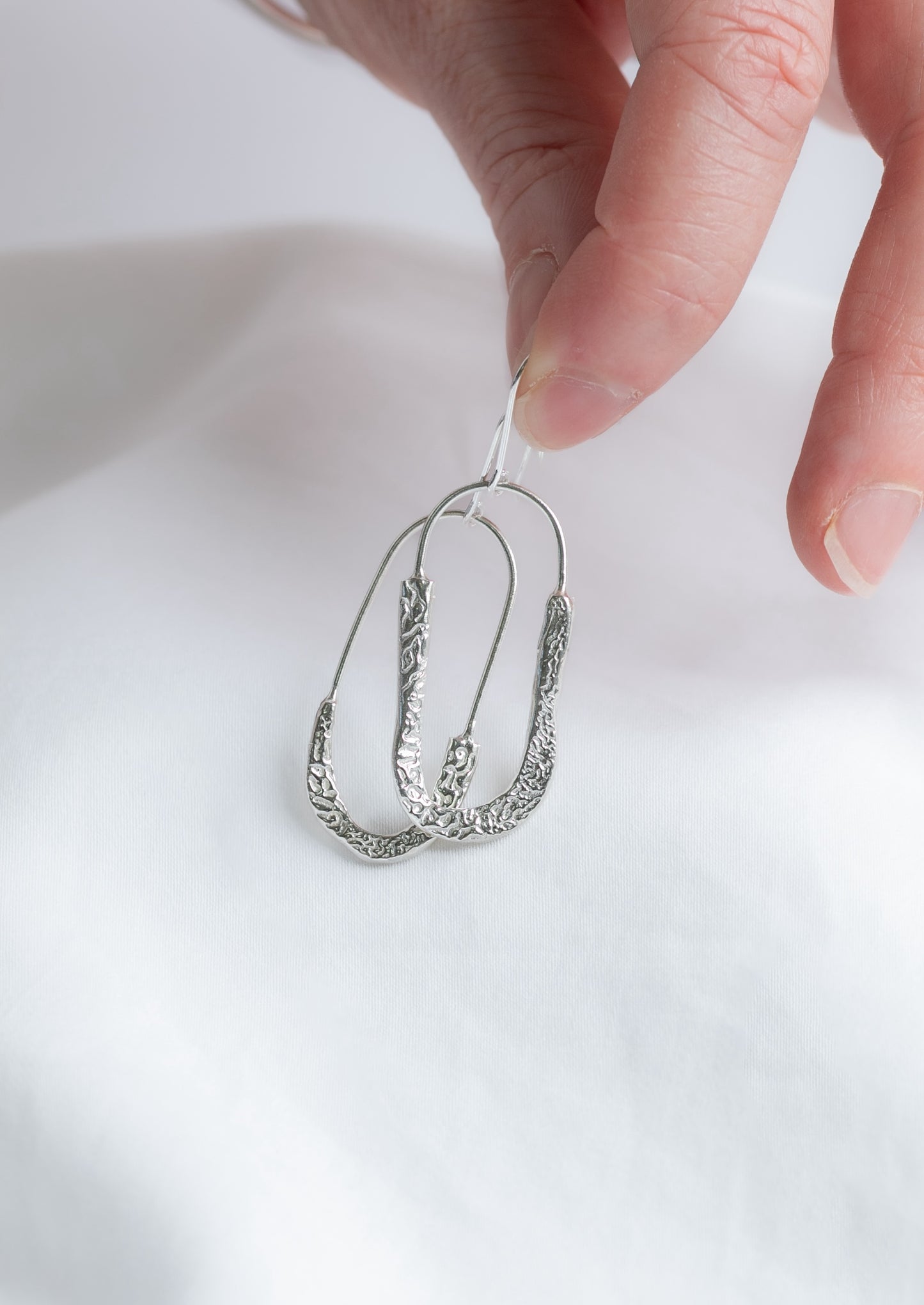 Silver cuttlefish textured earring held by a hand against a white background