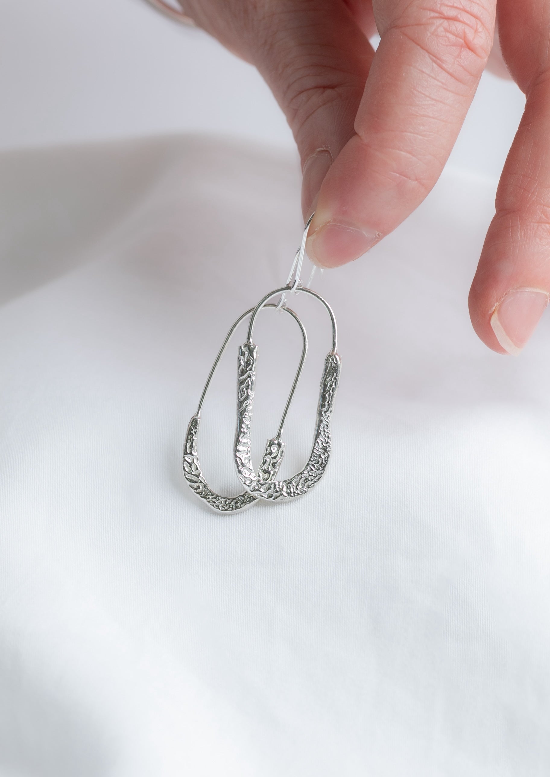 Silver cuttlefish textured earring held by a hand against a white background