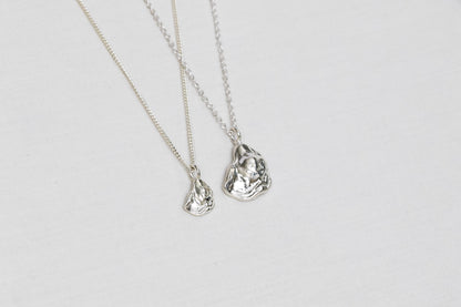 Two oyster necklaces lay side by side, one mini size and one larger size, both handmade from sterling silver