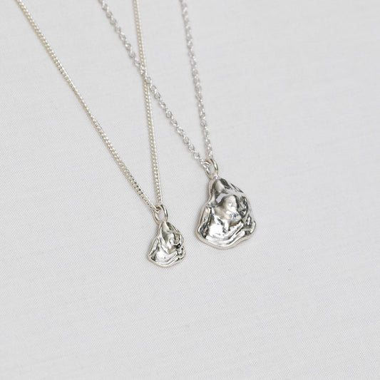 Two oyster necklaces lay side by side, one mini size and one larger size, both handmade from sterling silver