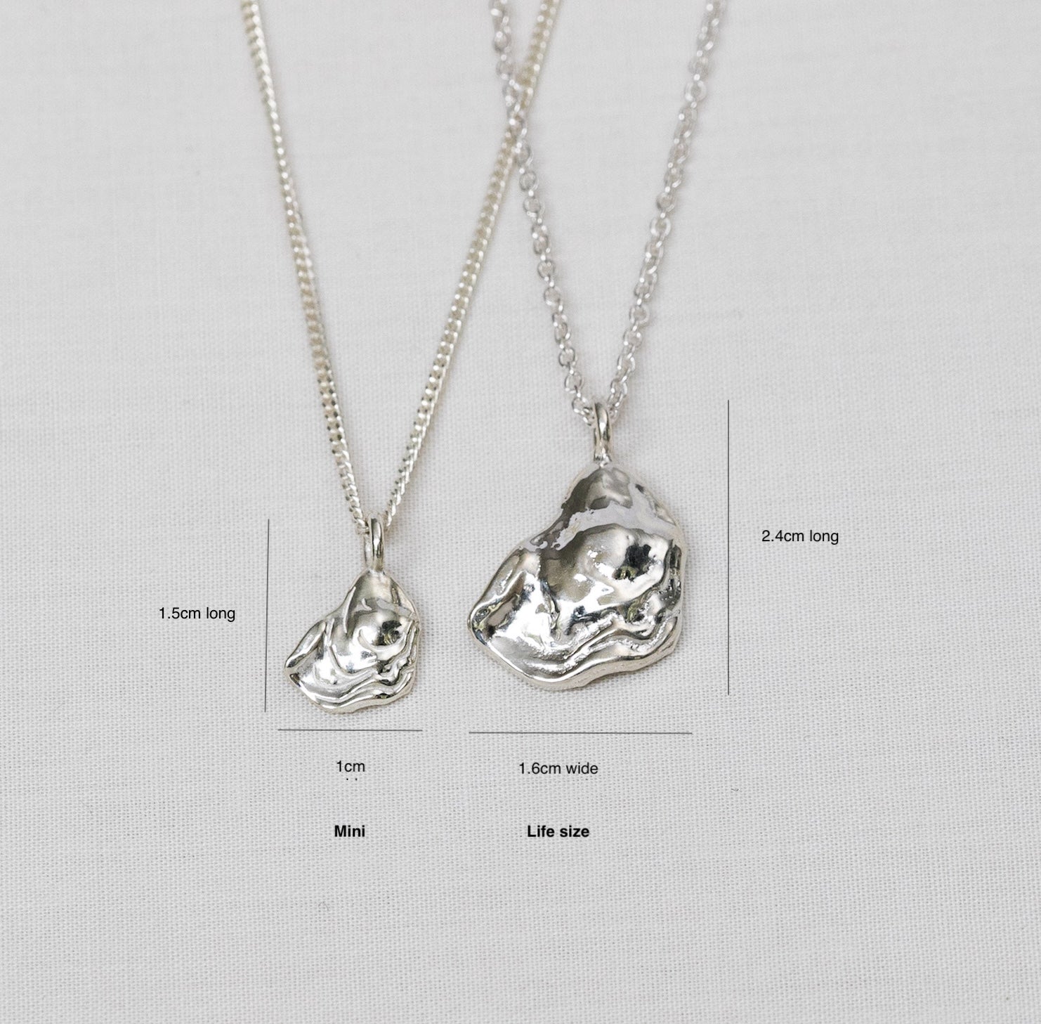 Two silver oyster necklaces lay side by side, one smaller than the other, both with measurements included for size comparison