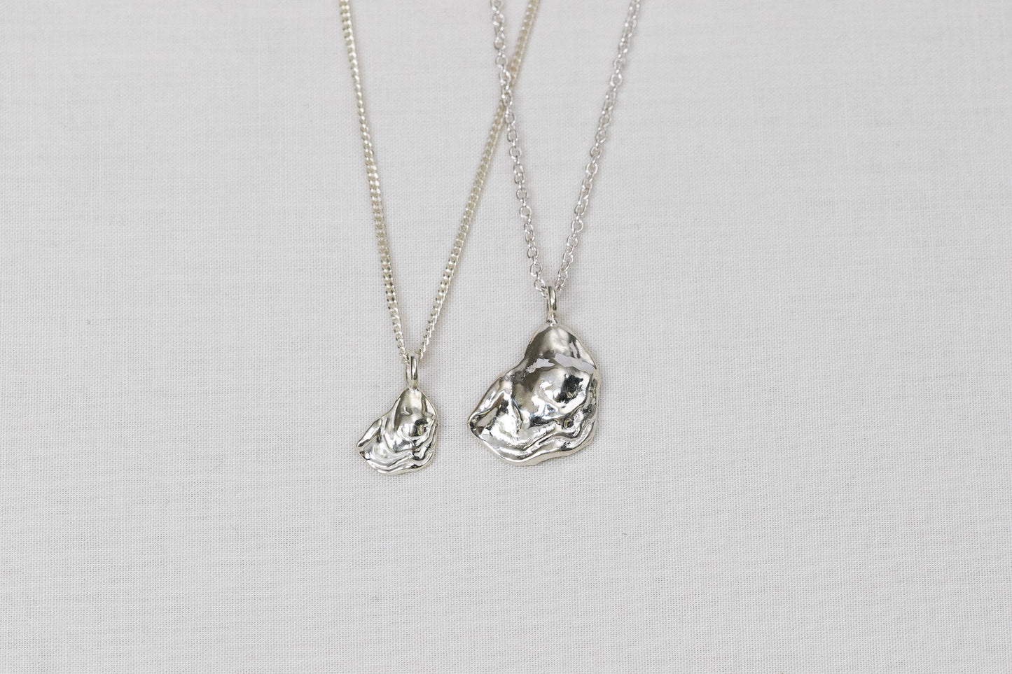 Two silver necklaces with oyster lid pendants on a light background.