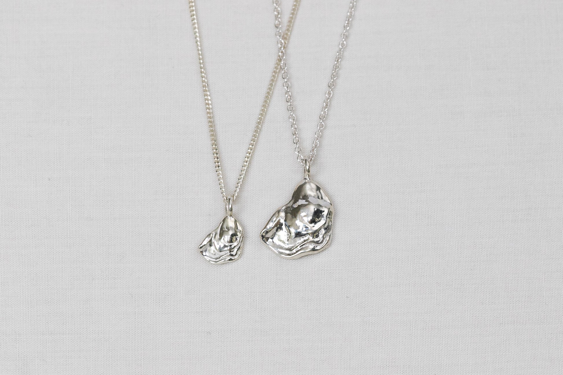 Two silver necklaces with oyster lid pendants on a light background.
