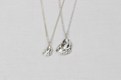 Two silver necklaces with oyster lid pendants on a light background.