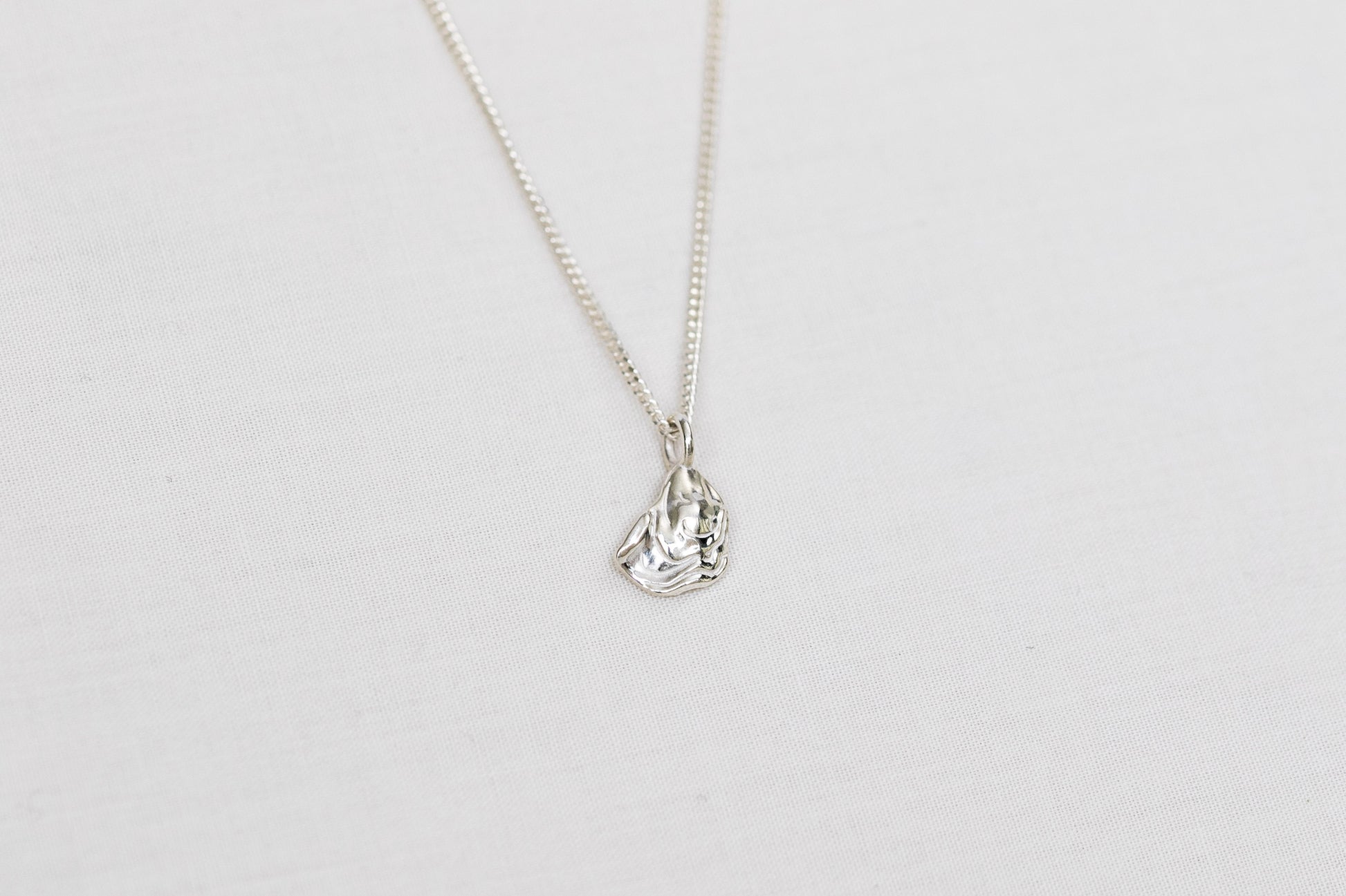 A small silver oyster pendant necklace on a light background