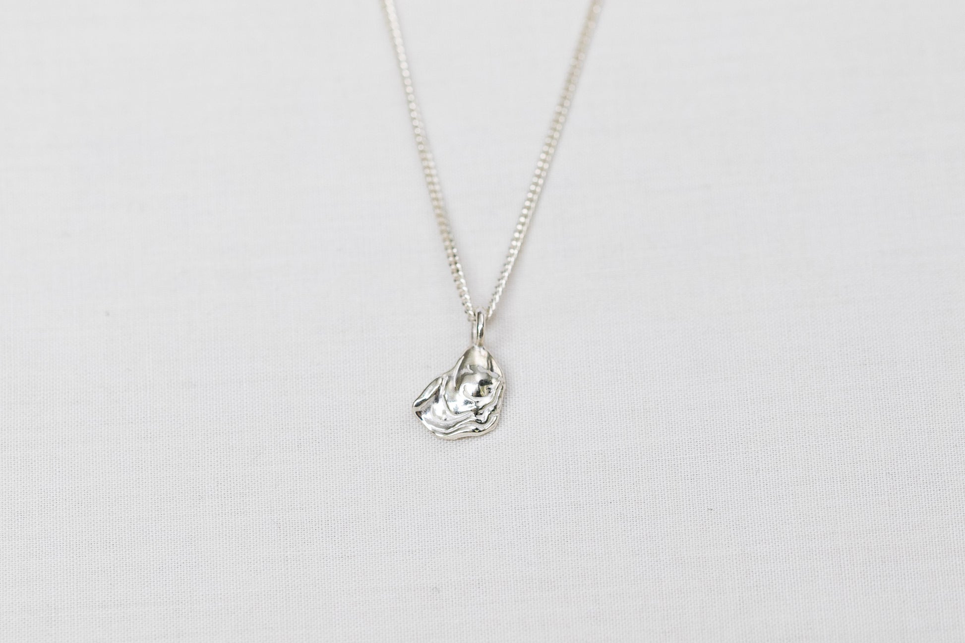 Mini sterling silver oyster pendant necklace sits centred on a light background
