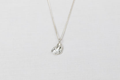 Mini sterling silver oyster pendant necklace sits centred on a light background