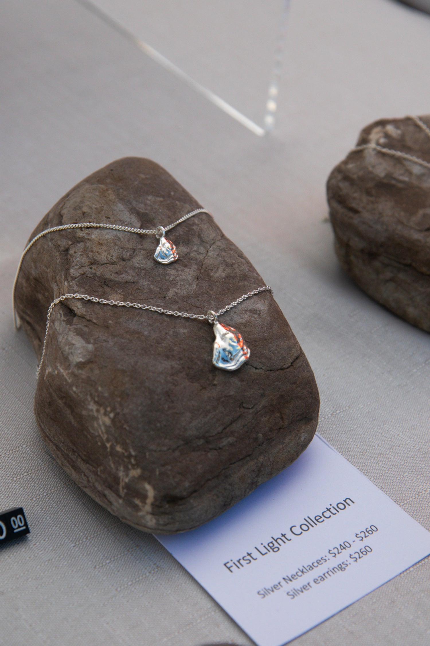 Two silver oyster necklaces lay on a rock, one larger than the other, handcrafted from sterling silver