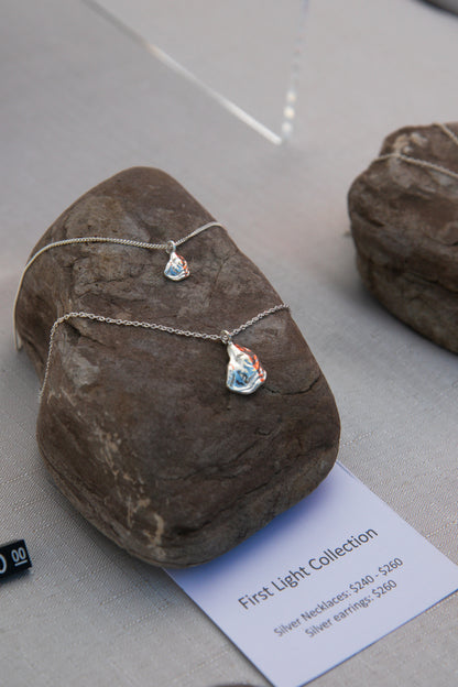 Two silver oyster necklaces lay on a rock, one larger than the other, handcrafted from sterling silver