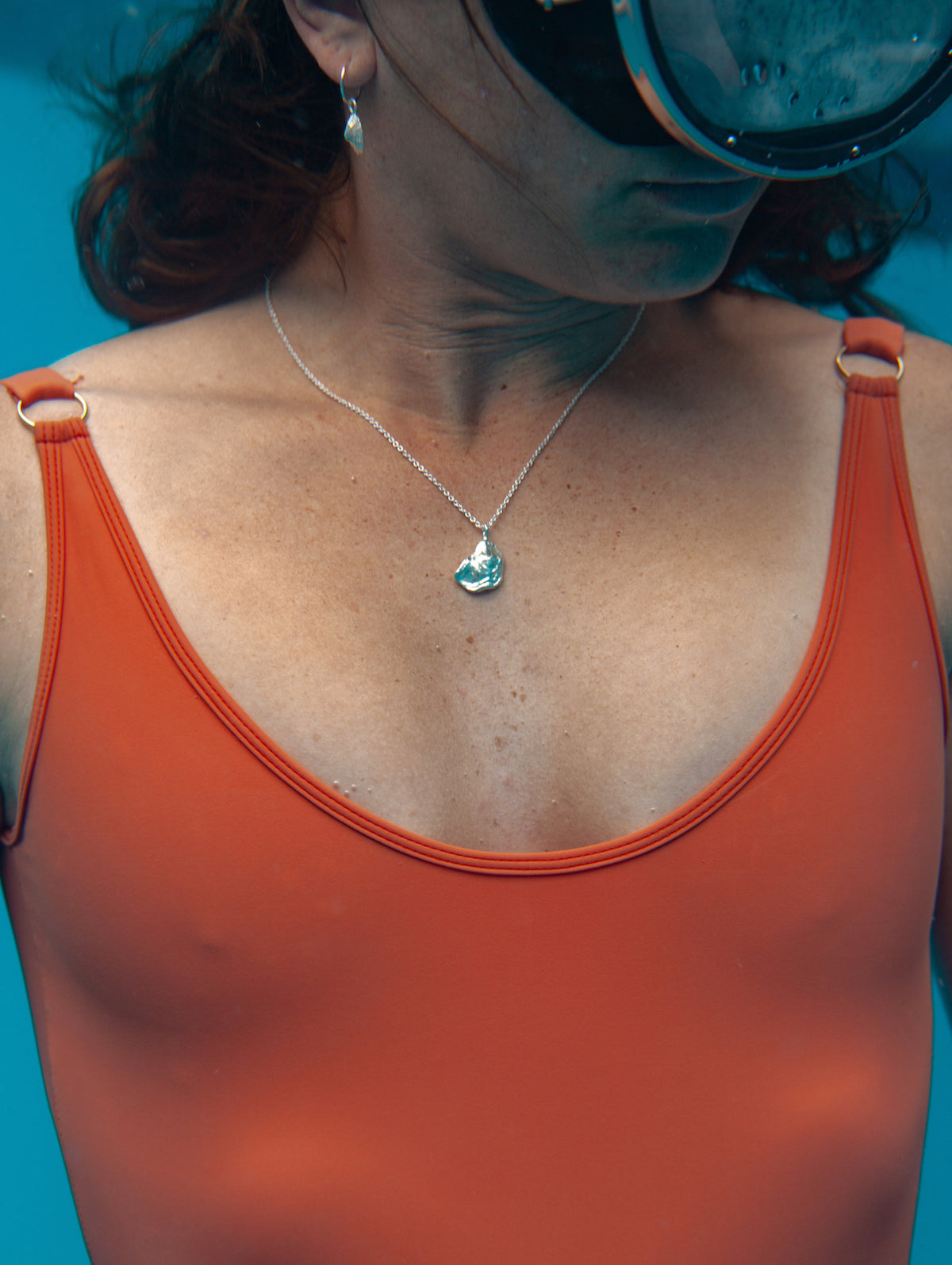 Model wears the large oyster necklace underwater in red swimsuit
