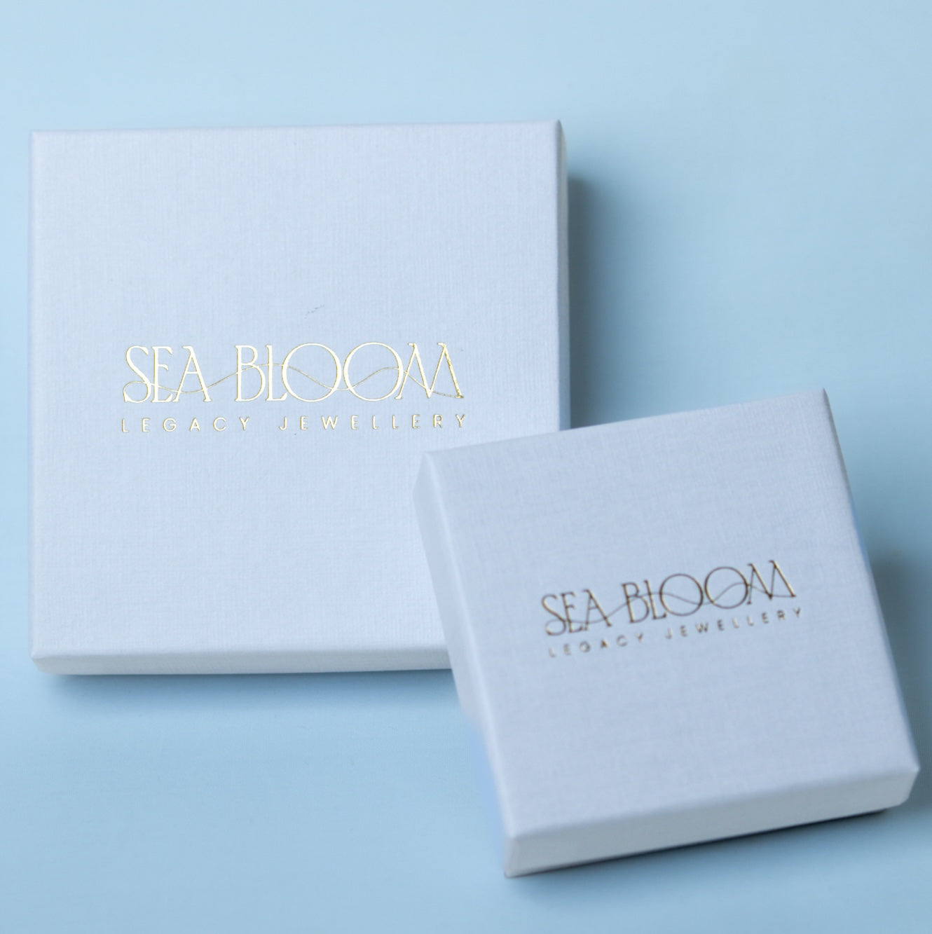 Two white jewelry boxes with 'Sea Bloom' branding on a light blue background