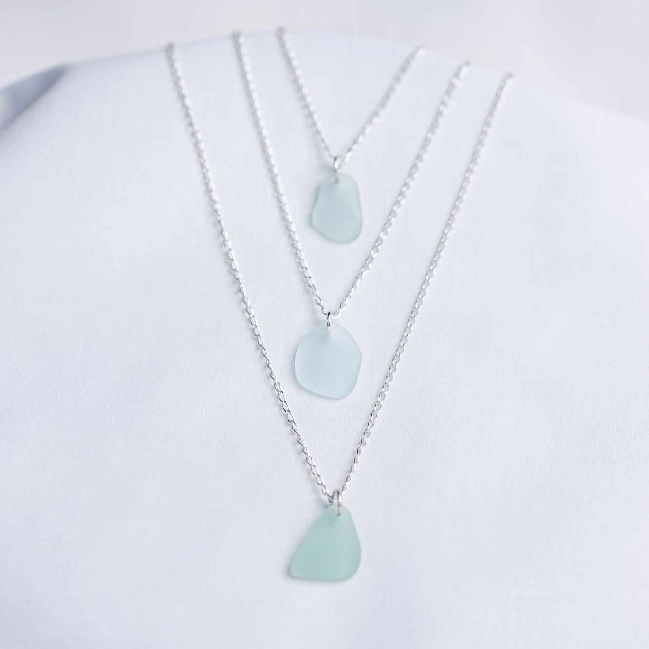 Three light blue sea glass pendant necklaces on a white background