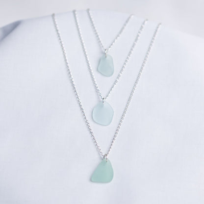 Three light blue sea glass pendant necklaces on a white background