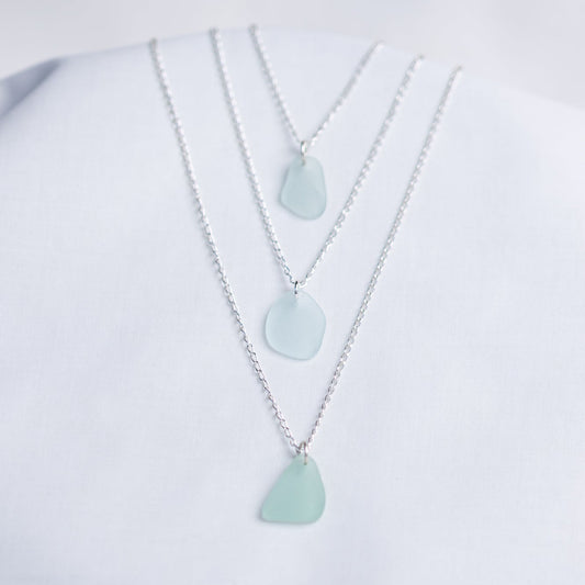 Three light blue sea glass pendant necklaces on a white background