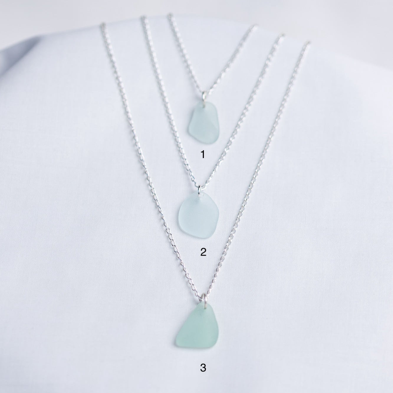 Three necklaces with light blue sea glass pendants on a white background