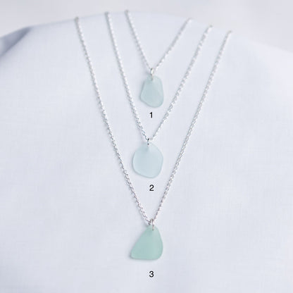 Three necklaces with light blue sea glass pendants on a white background
