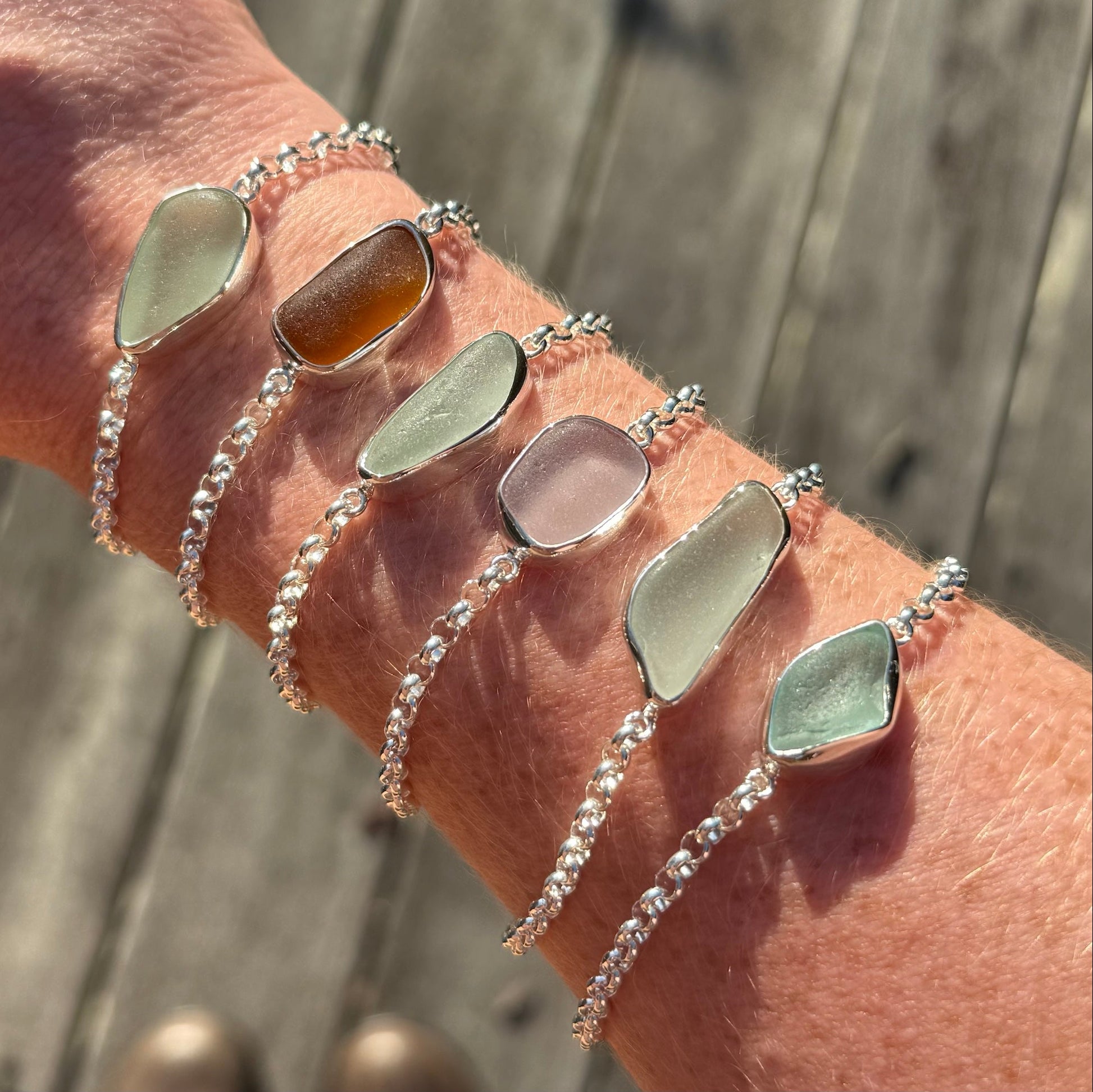 Six sea glass bracelets of different colours shine in the sun being worn on an arm